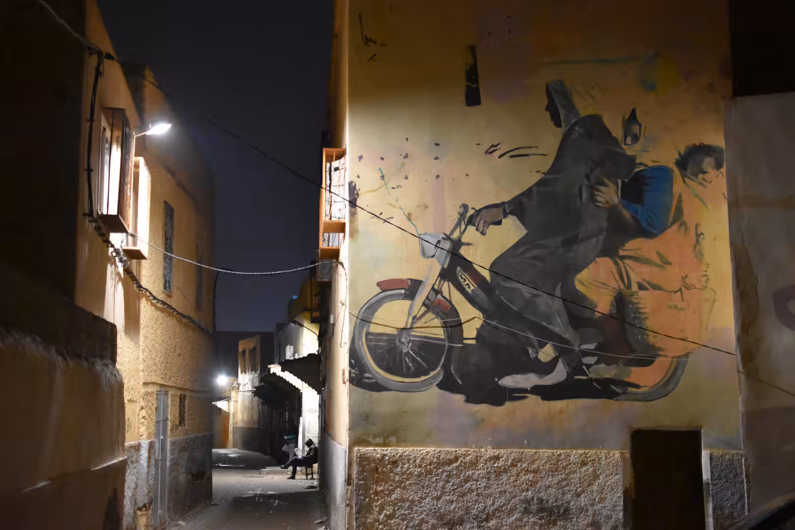 Large mural of a rider on a scooter painted on a wall in a narrow alley at night.