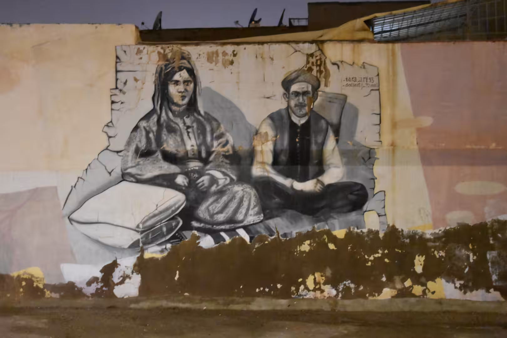 Black-and-white mural depicting two people in traditional clothing on a city wall.