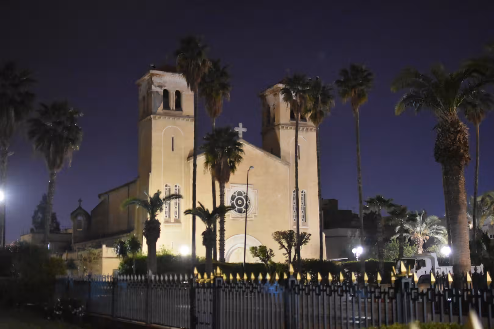 Historic cathedral illuminated at night and surrounded by palm trees in Oujda, Morocco.