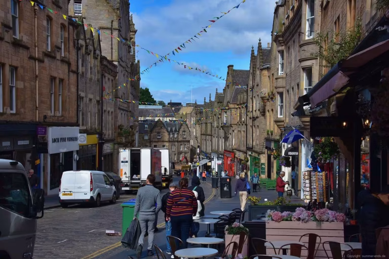 Stone tenement facades line a lively street crisscrossed by strings of colorful bunting.