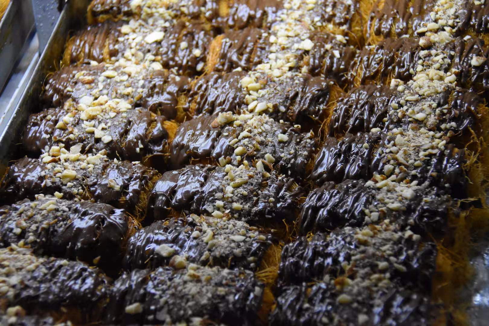 Close-up of chocolate-coated pastries topped with chopped nuts and arranged in a bakery tray.