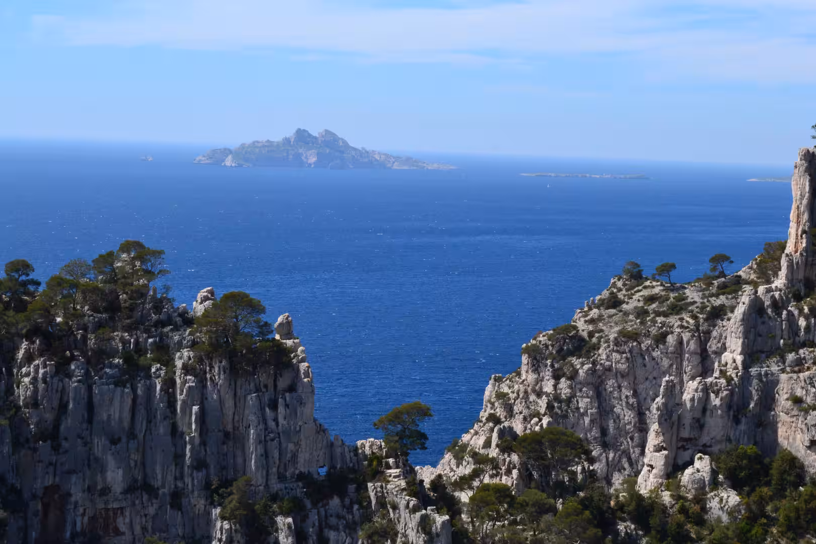 Deep blue Mediterranean with a rocky island on the horizon, cliffs and pines below