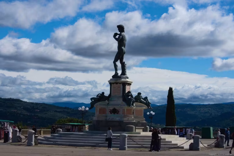 A bronze copy of Michelangelo's David stands on a monument above a terrace overlooking rolling hills.