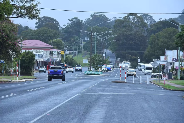 A quiet rural main street lined with shops leads up to green wooded hills.