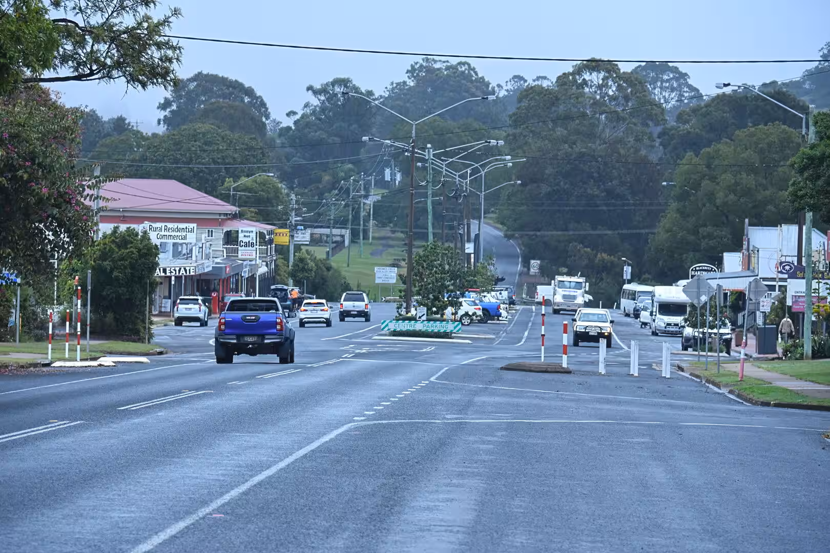 A quiet rural main street lined with shops leads up to green wooded hills.