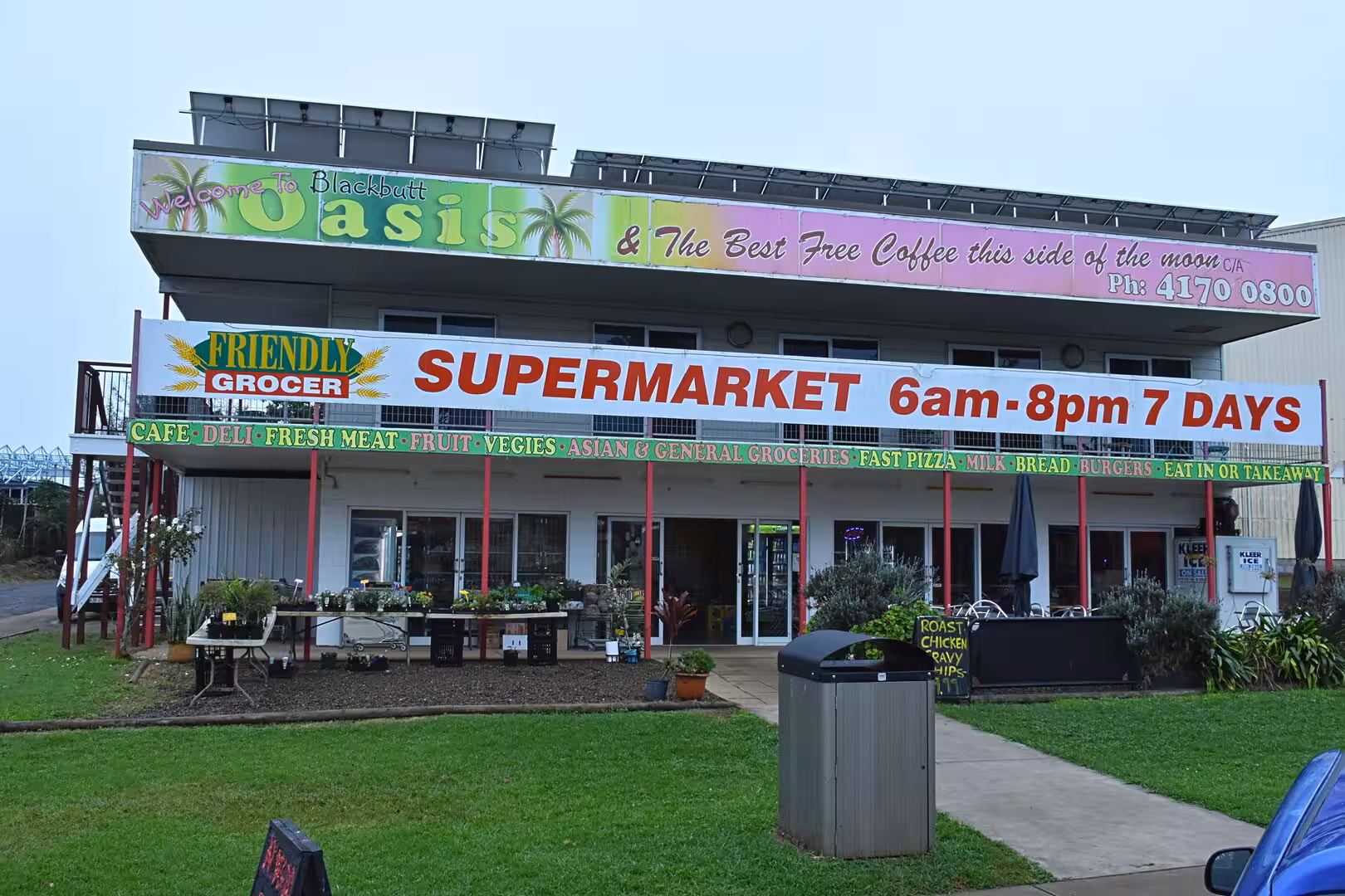 A friendly grocer supermarket displays bright signage and potted plants out front.