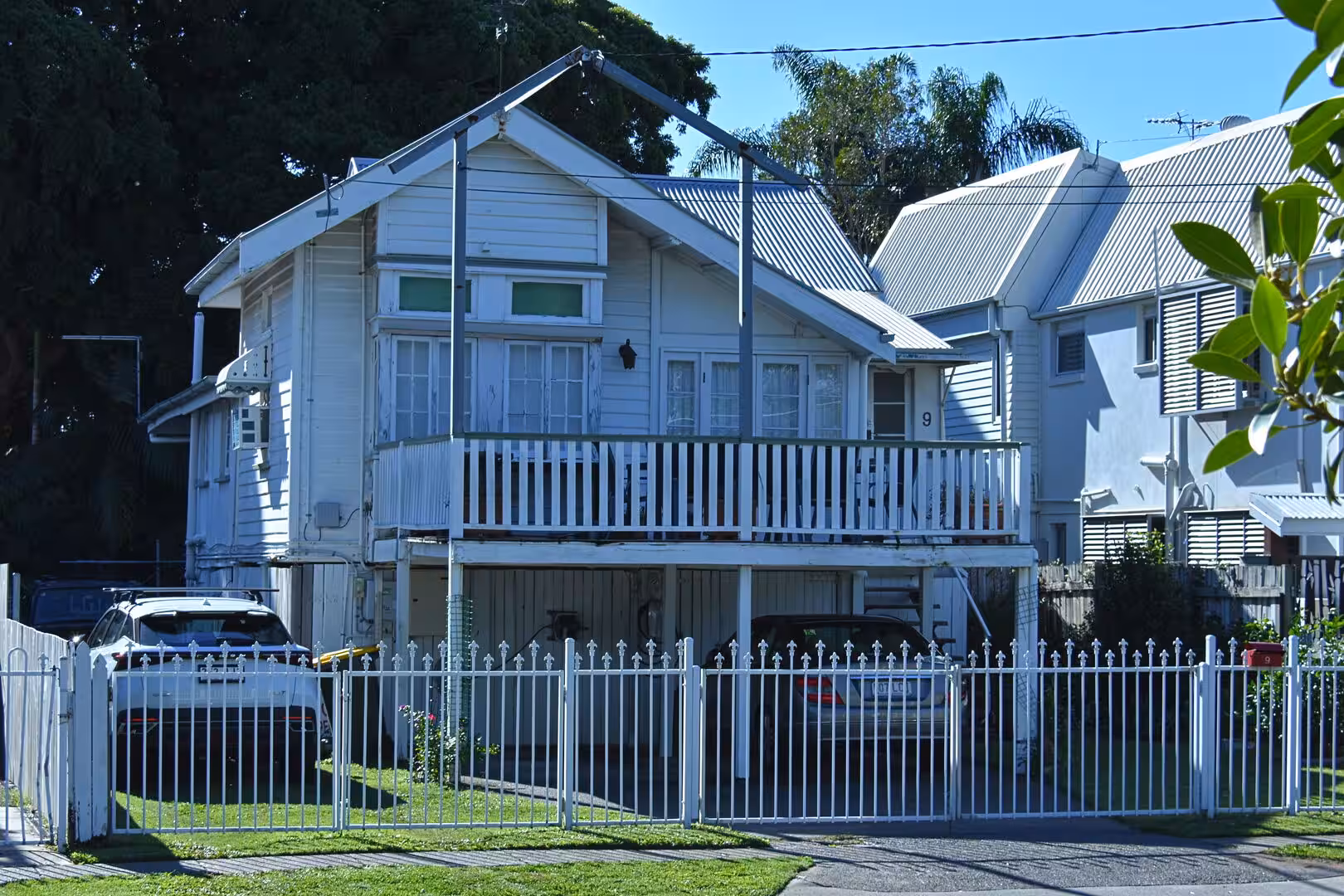 A classic white weatherboard house with a full-width balcony behind a white picket fence.