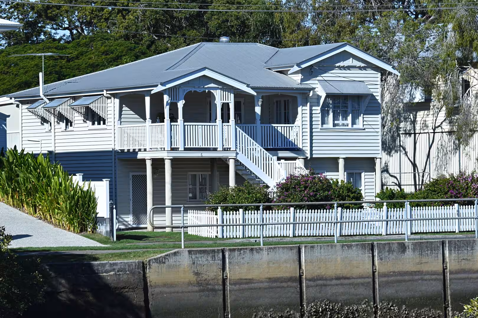 An ornate white house with a decorated balcony, an external stair, and a white picket fence.