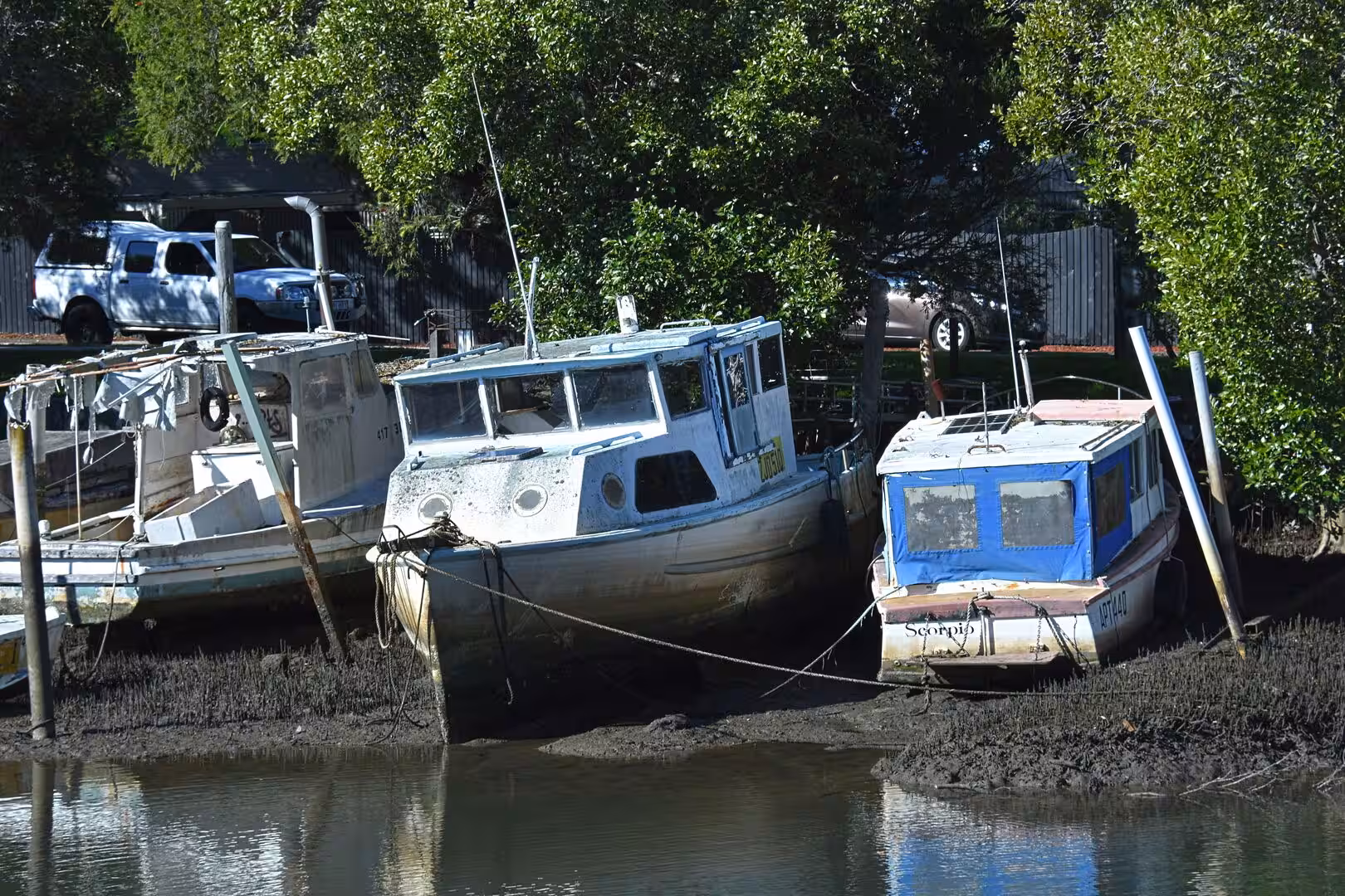 Three salt-worn fishing boats sit high and dry on a muddy riverbank at low tide.