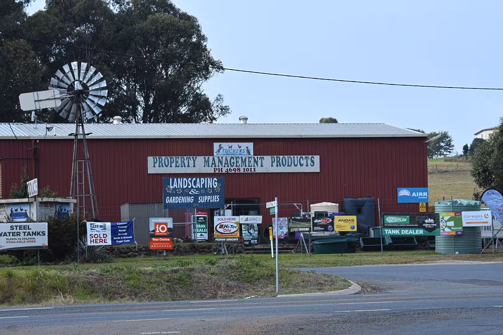 A red tin building selling landscaping and gardening supplies stands beside a tall windmill.