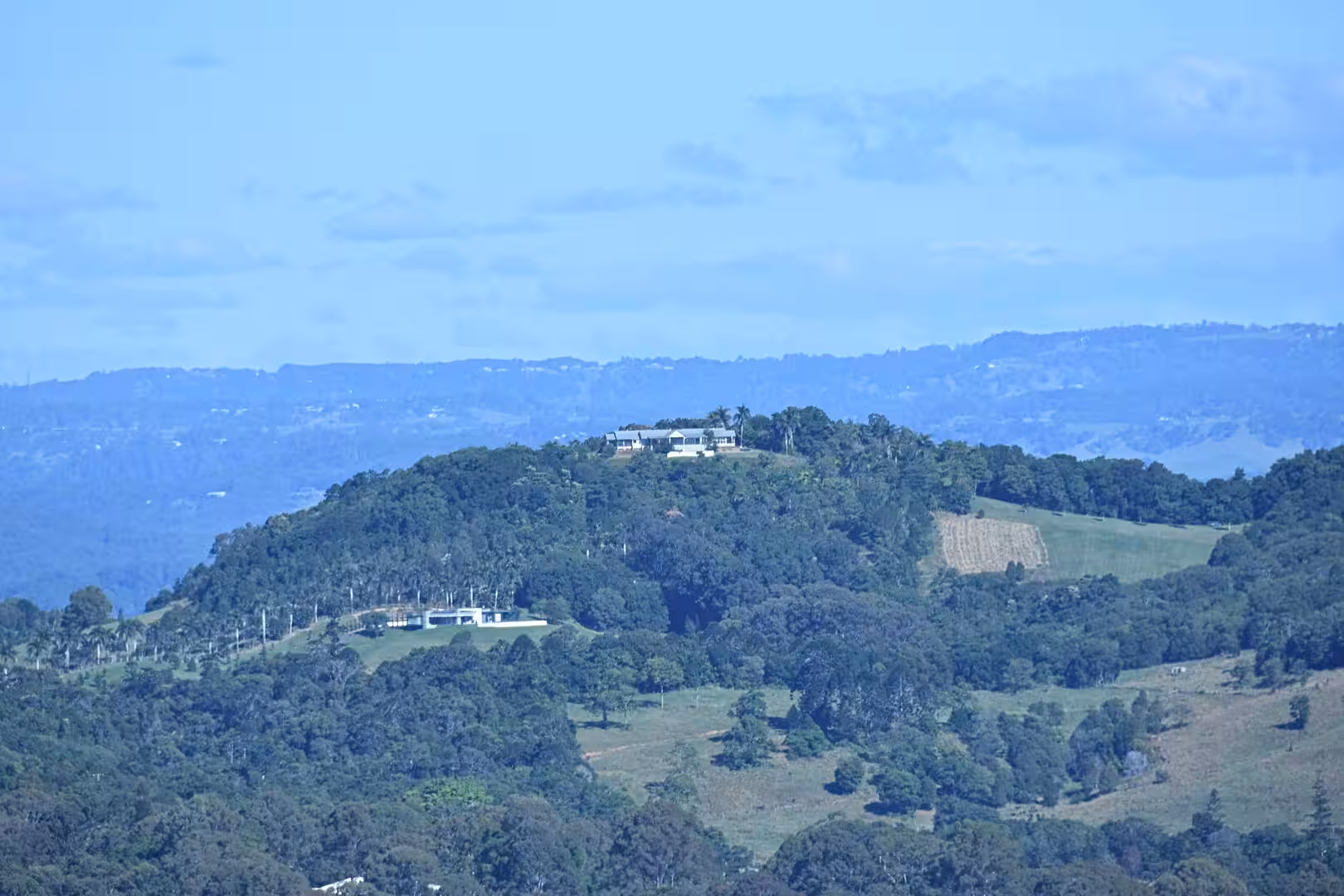 A lone white house perches on a forested, sunlit hilltop.
