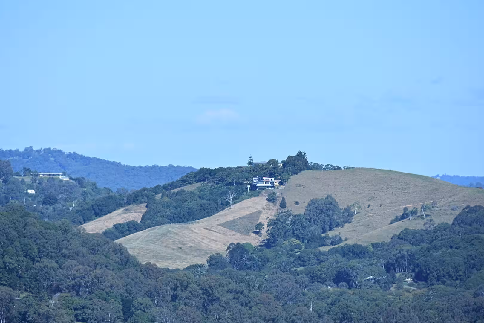 Sunlit fields and forest roll across gentle hills under a blue sky.