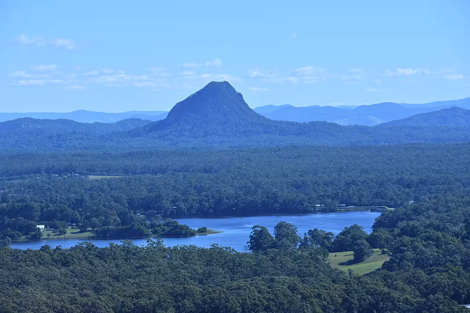 A sharp volcanic-looking peak rises behind a forested lake.