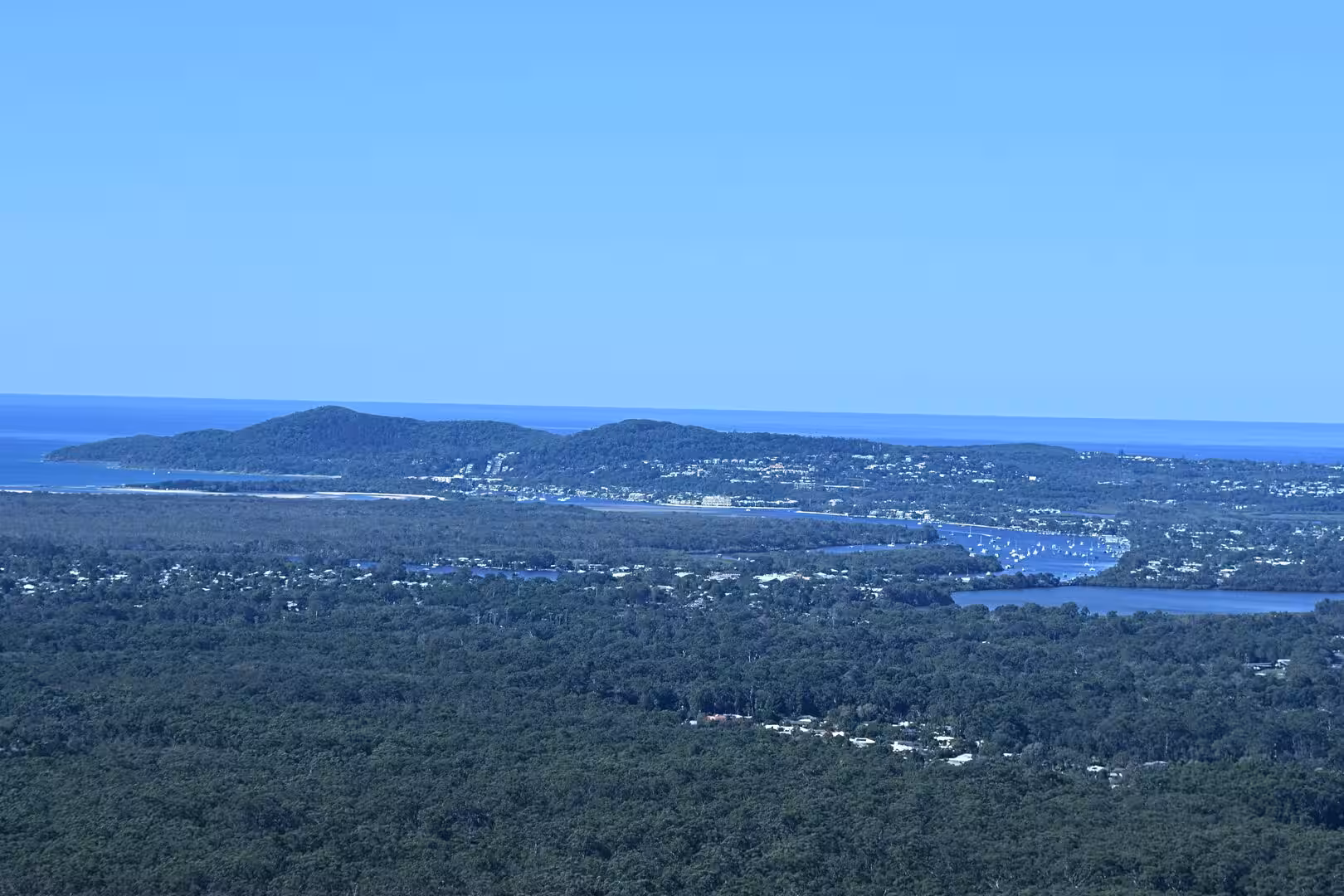 A bright aerial view of a coastal settlement around a boat-dotted estuary.