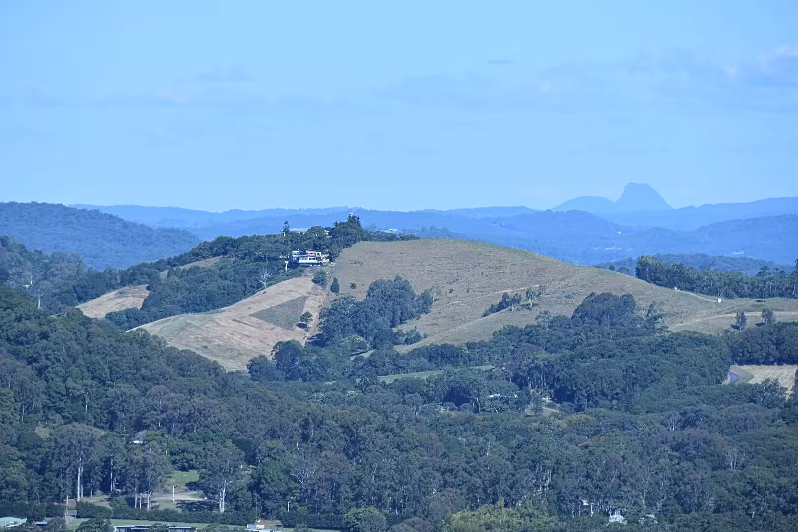 Houses crowned on a green ridge above grassy paddocks and wooded hills.