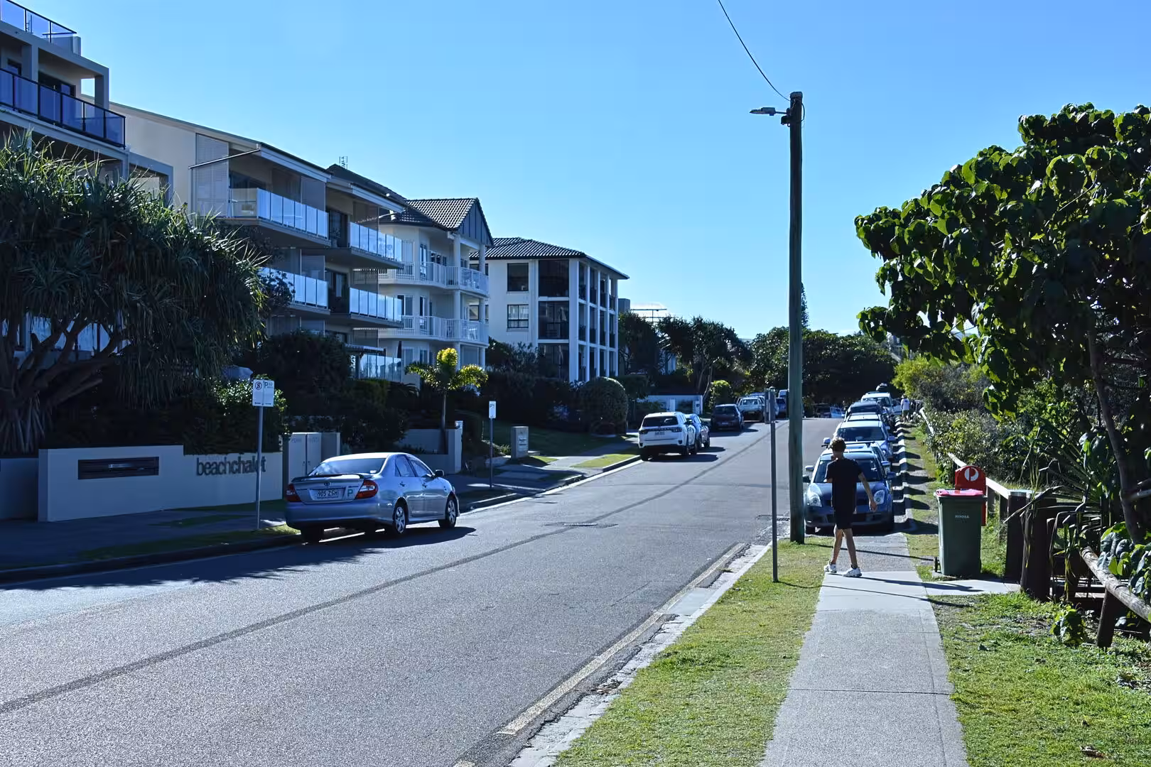 A straight suburban street lined with white apartment blocks and parked cars.