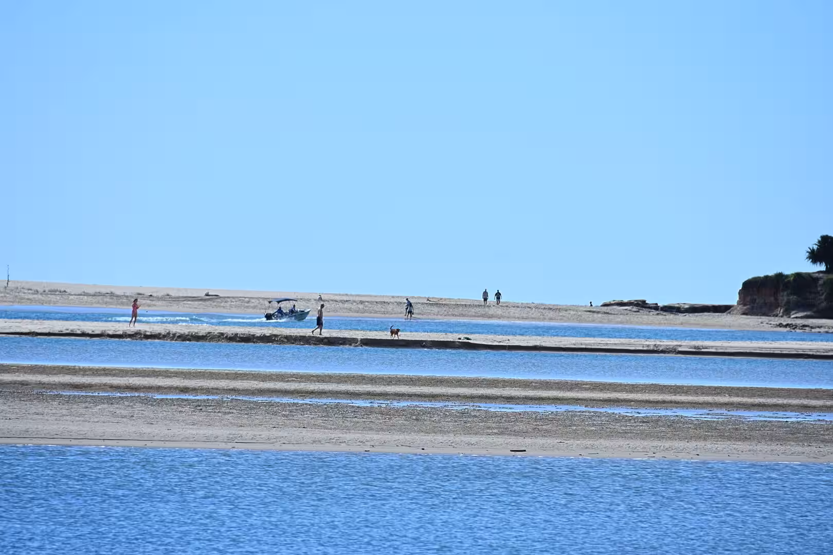 Shallow tidal channels weave through pale sandbars towards a small boat