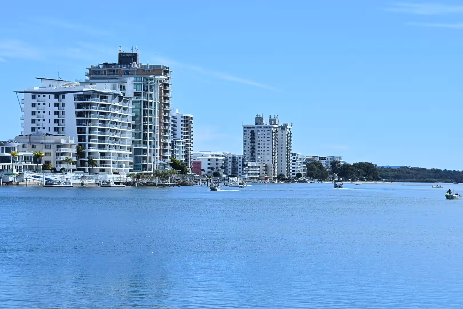 A row of modern apartment towers rises behind a marina and calm water