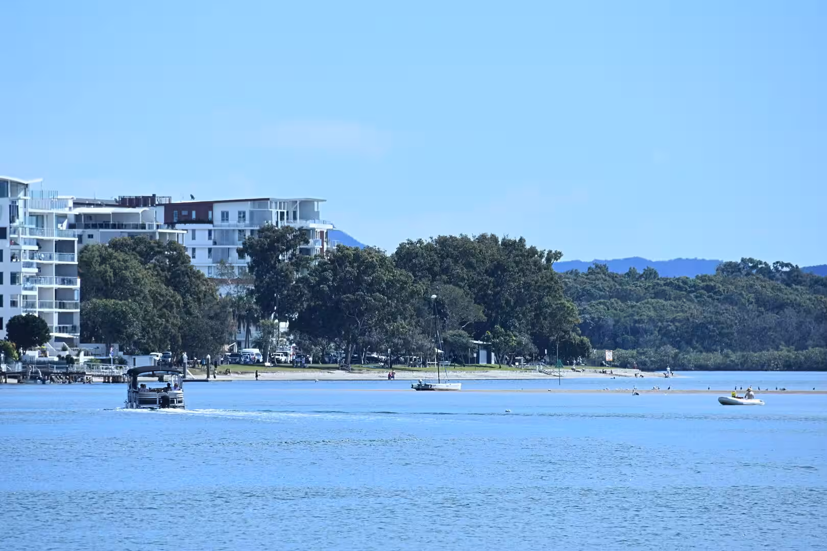 Apartment towers and a tree-lined shore face a wide calm river