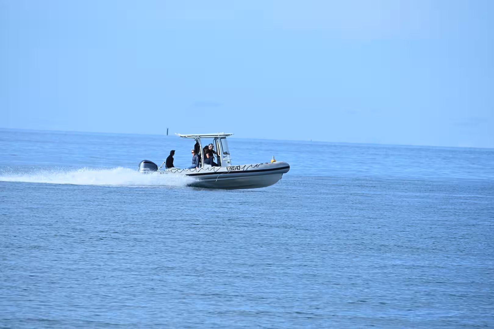 A white motorboat carrying several passengers races over calm water, trailing a bright wake behind it.