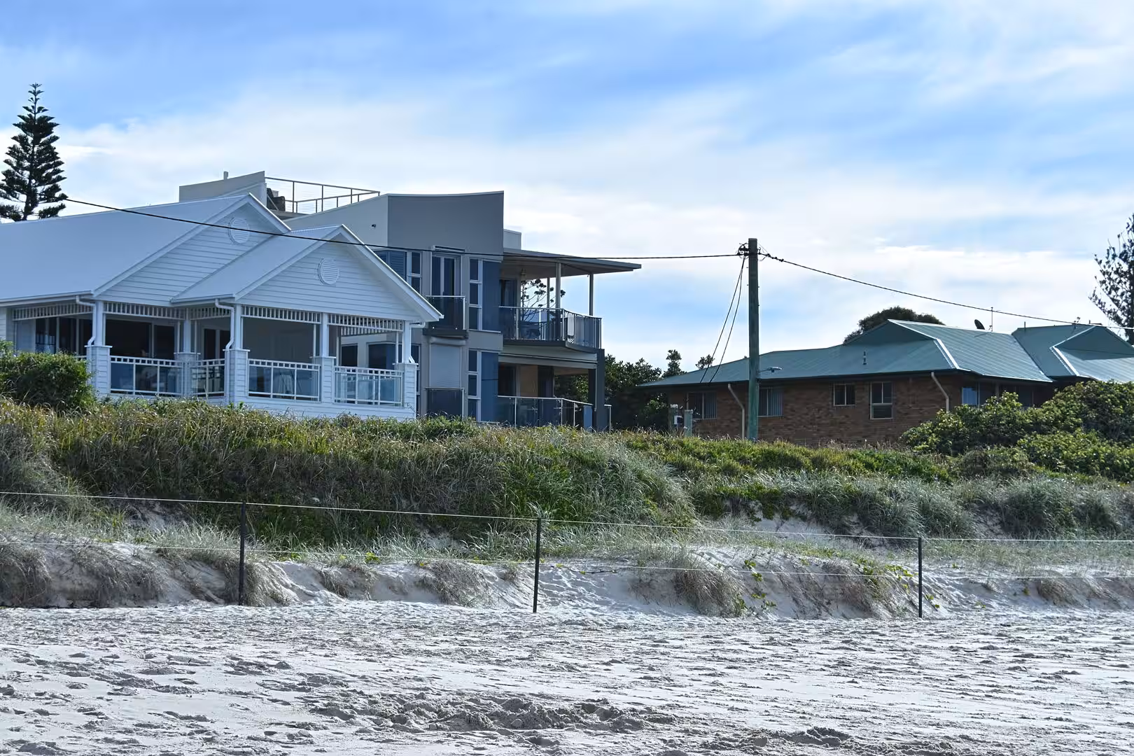 Coastal homes line a fenced dune above a sandy beach.