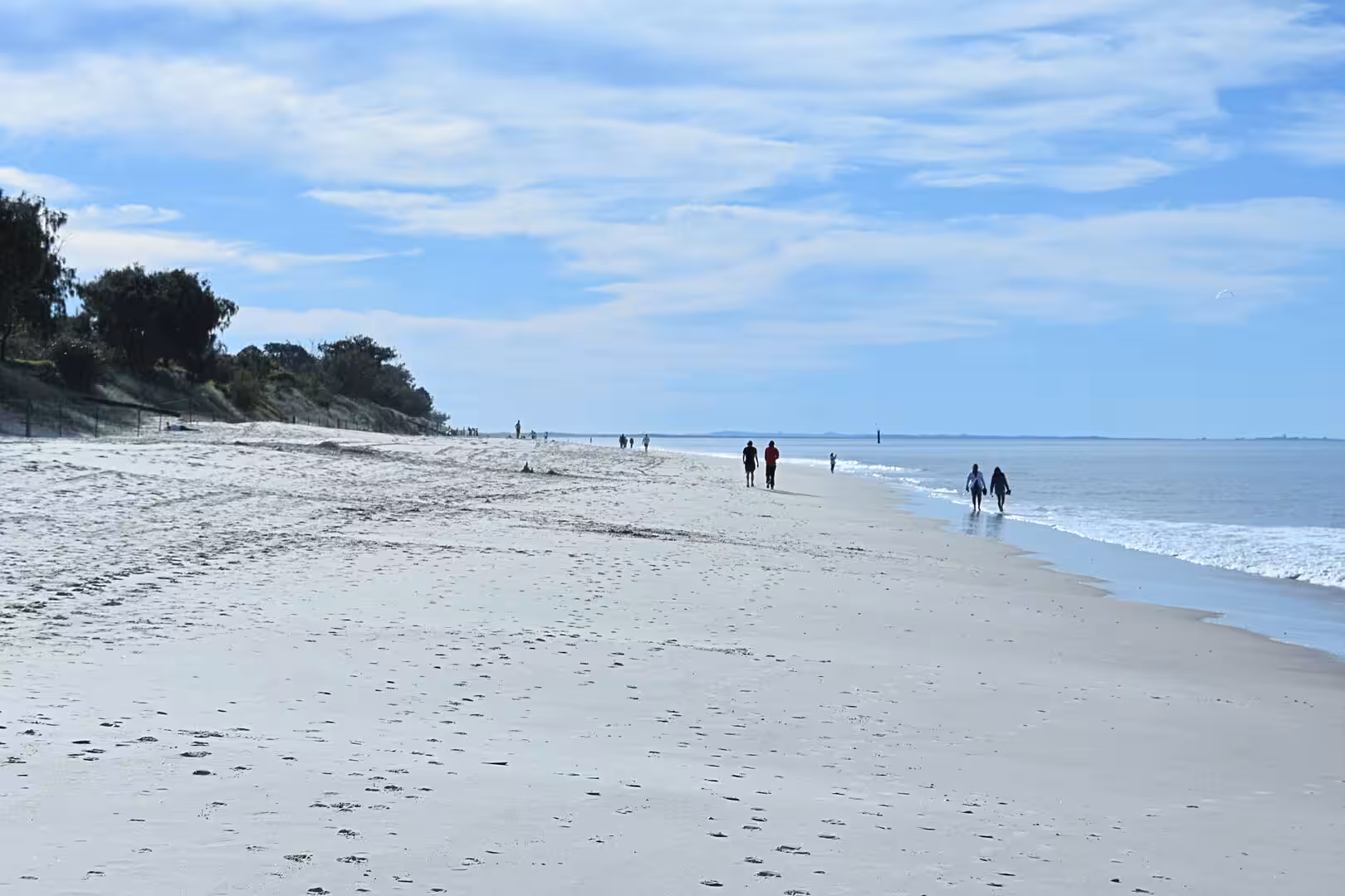 People walk the shoreline of a wide, curving beach.