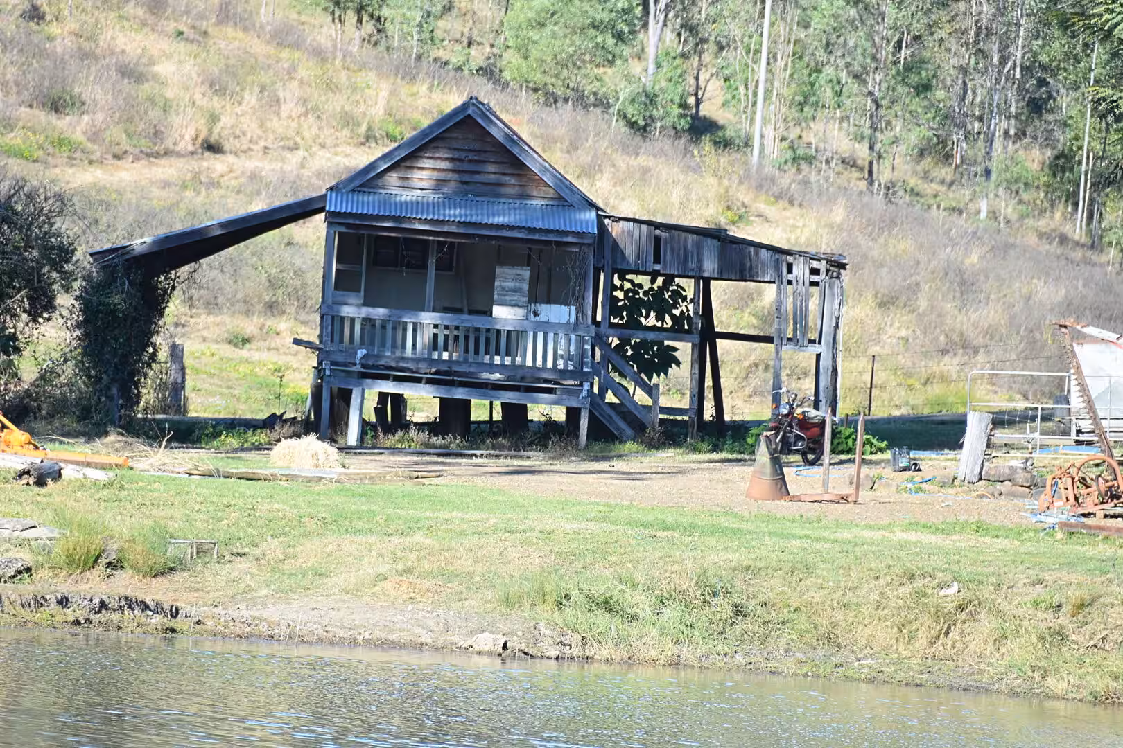 An old timber cabin sits on stumps above a grassy bank.