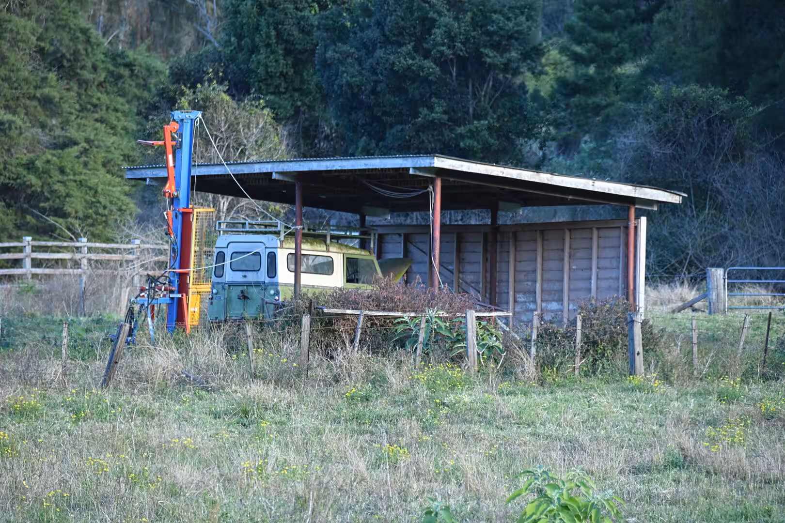 An old corrugated shed shelters a vintage truck behind a blue hoist crane.