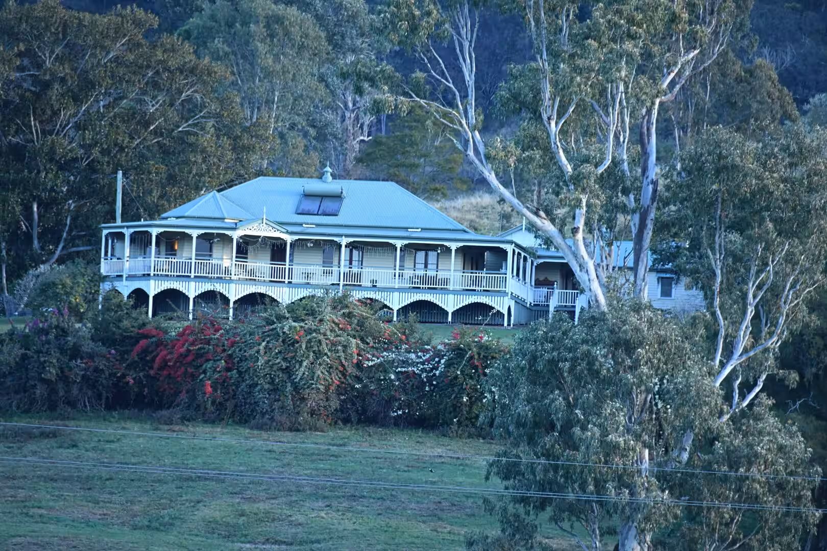 A grand white homestead with a wraparound verandah sits behind blooming bougainvillea.