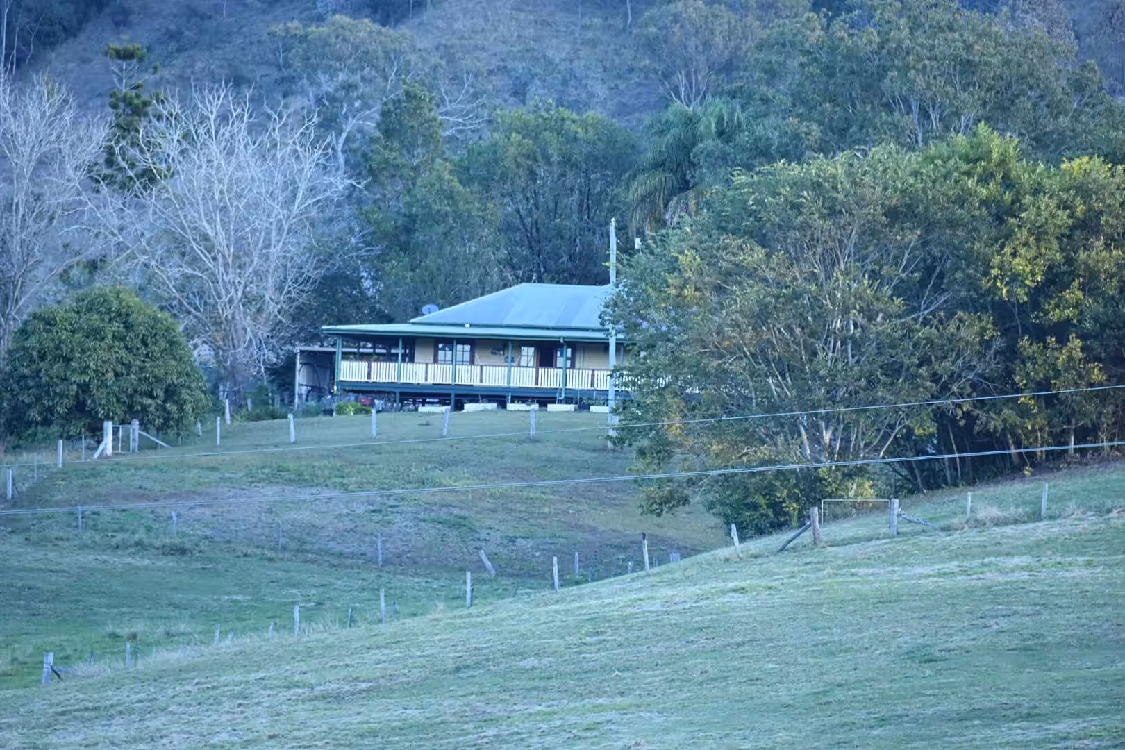 A single-storey home with a veranda sits on a grassy hillside.