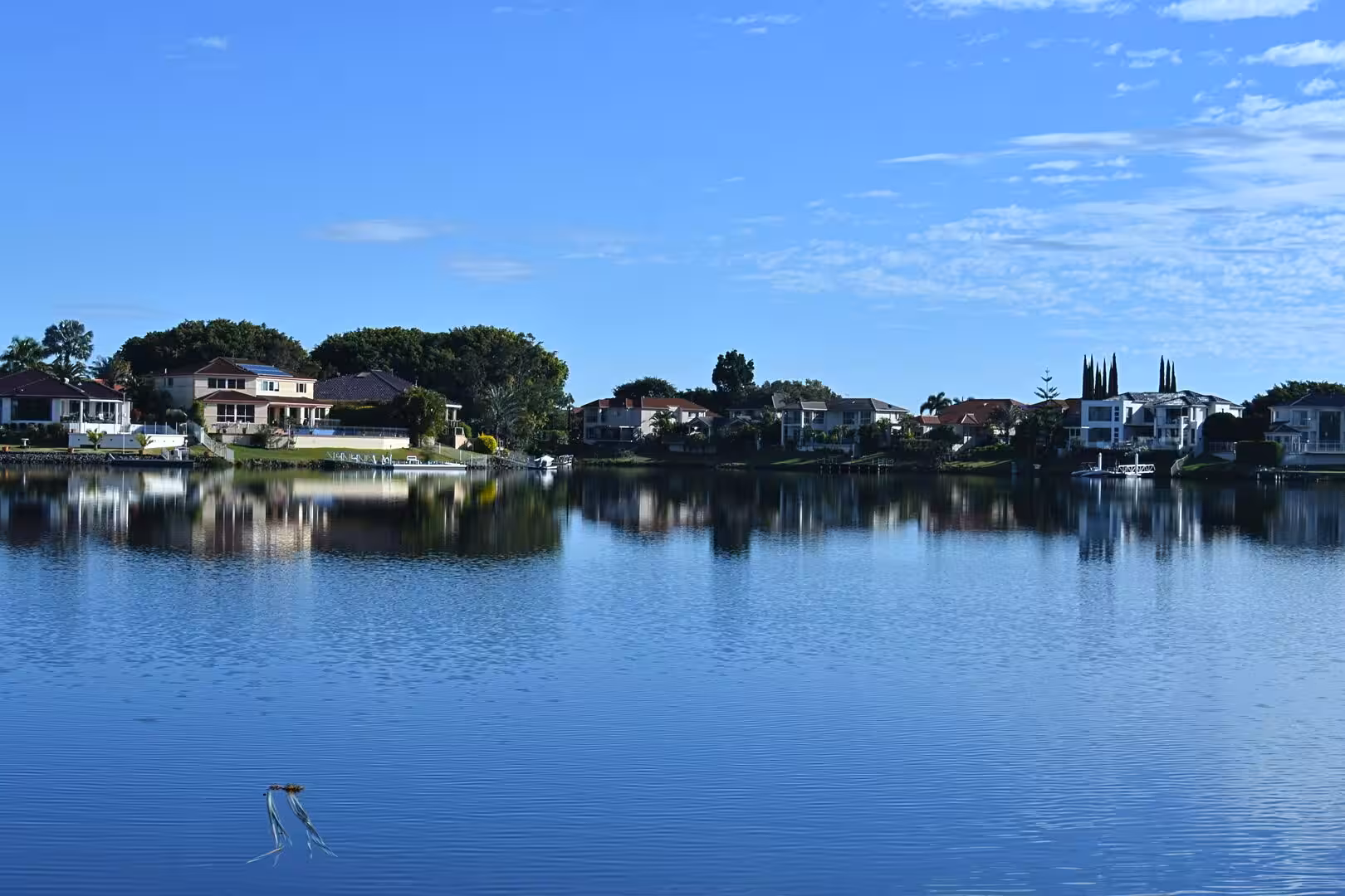Still blue water mirrors the houses lining a quiet residential riverfront.