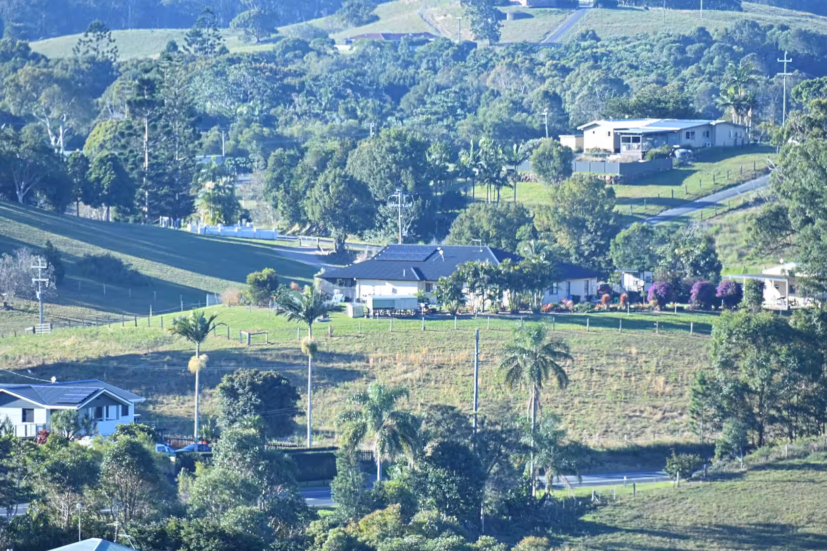 Rural houses and palm trees scatter across gently sloping green hillsides.