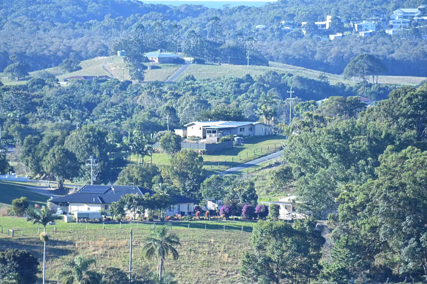 Farm houses rest on green hills with dense forest and distant ridge dwellings.