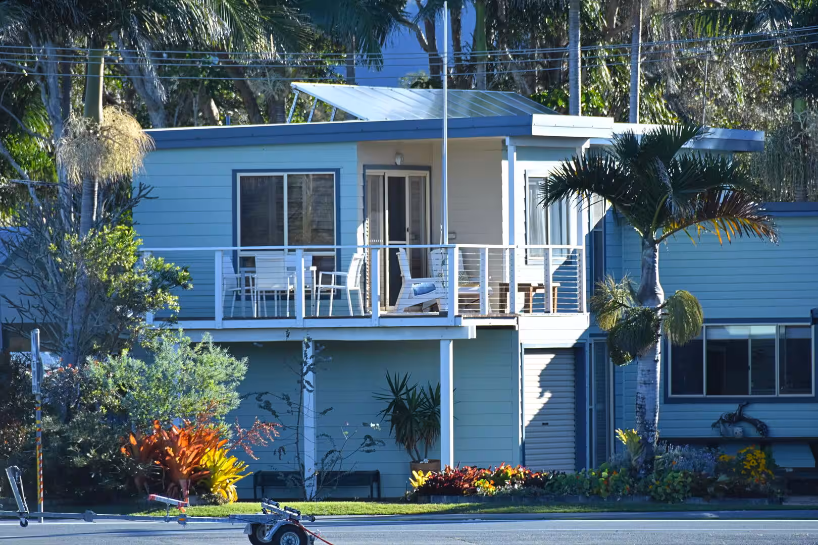 A light blue stilt house with a white balcony overlooks lush palms.