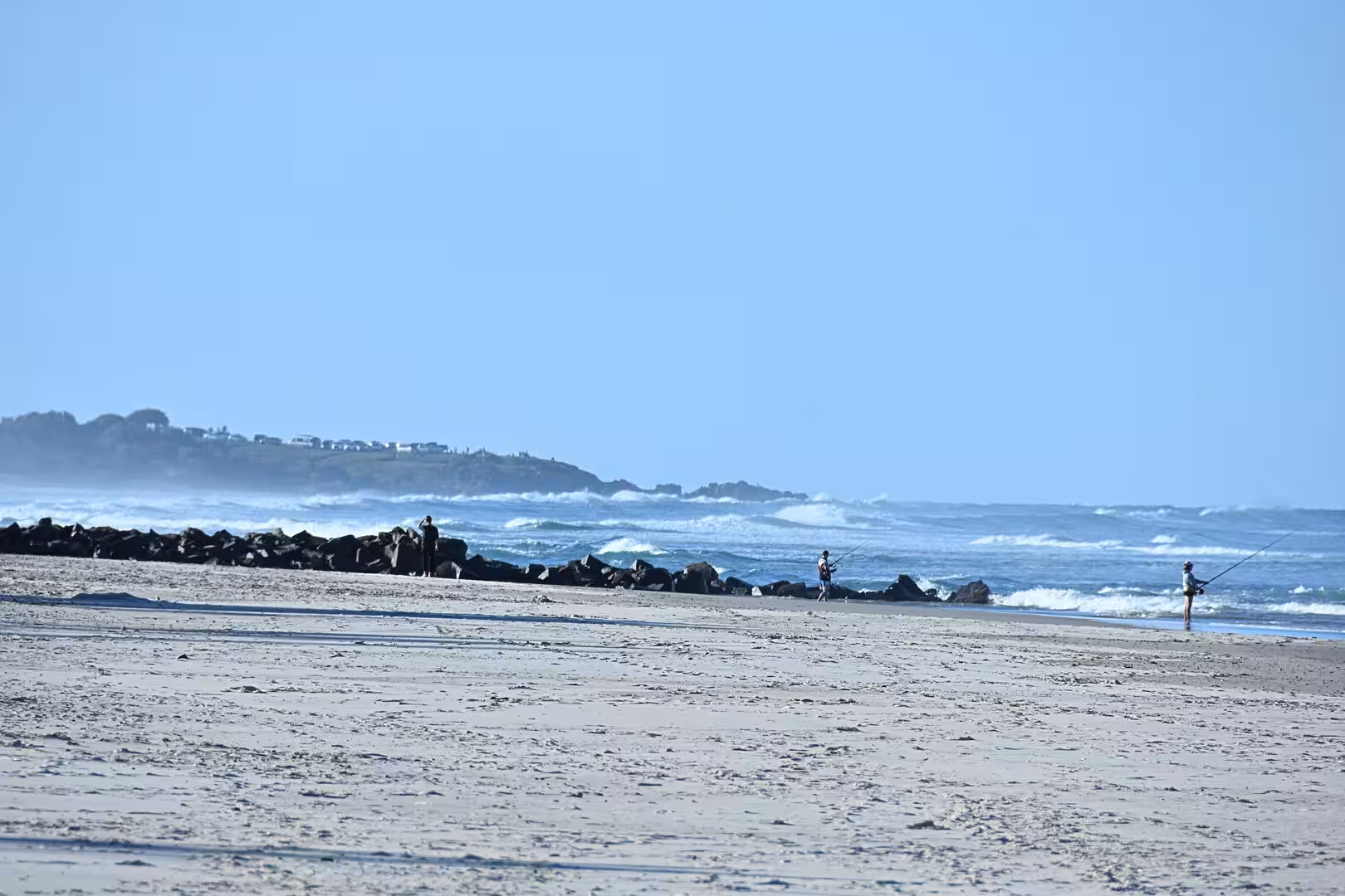Anglers cast lines from rocks at the water's edge.
