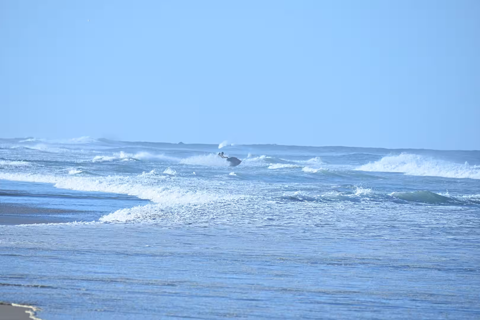 A pelican skims just above the breaking surf.