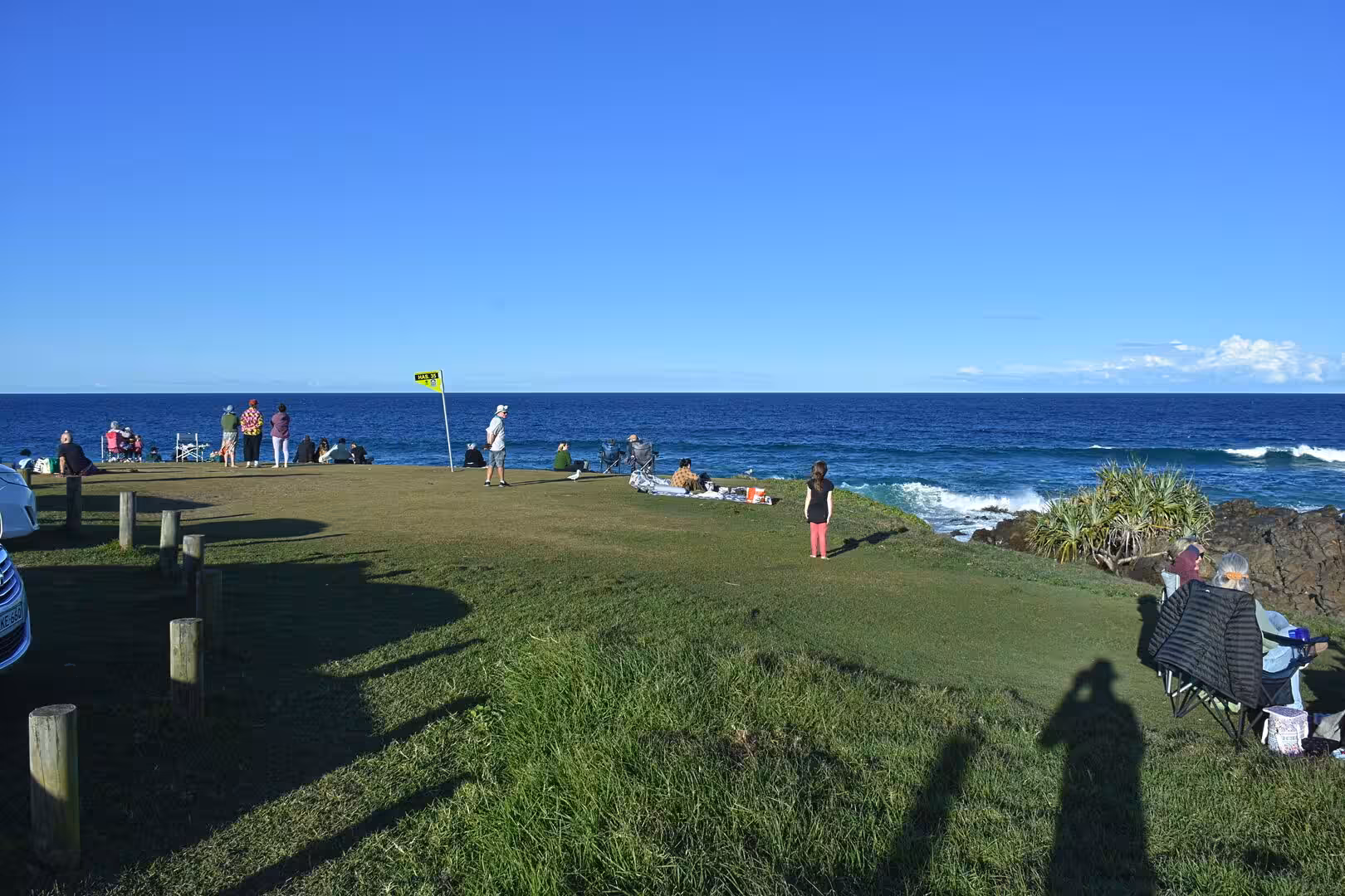 People gather on a grassy point overlooking the ocean.