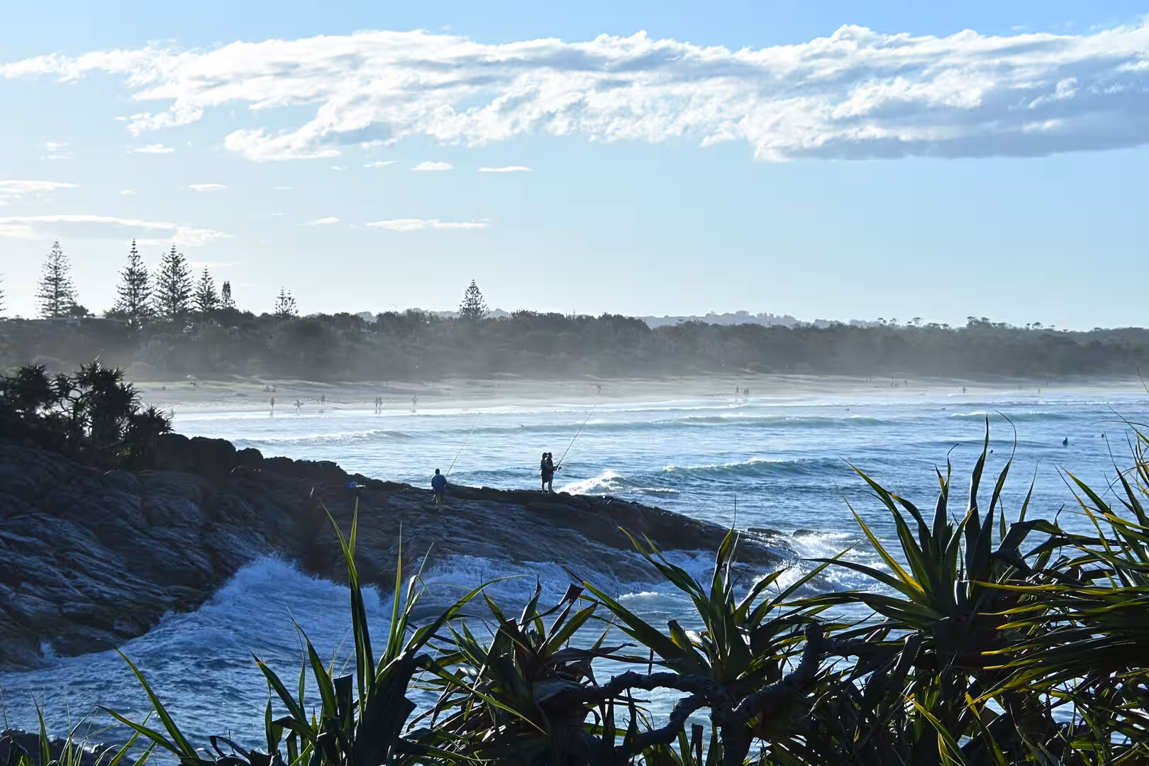 Fishermen cast their lines from a rocky point into rolling surf.