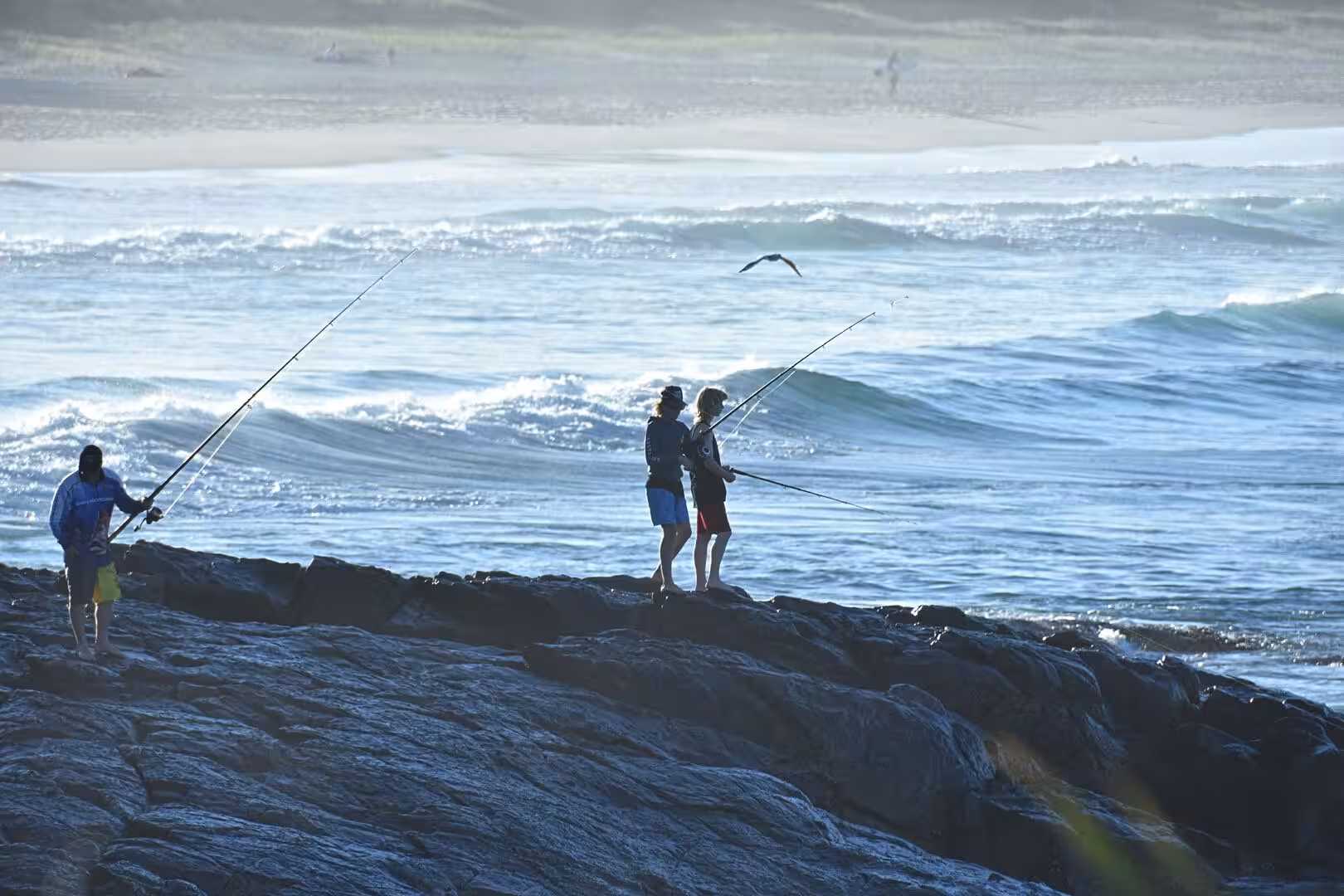 Silhouetted fishermen cast long rods over bright breaking waves.