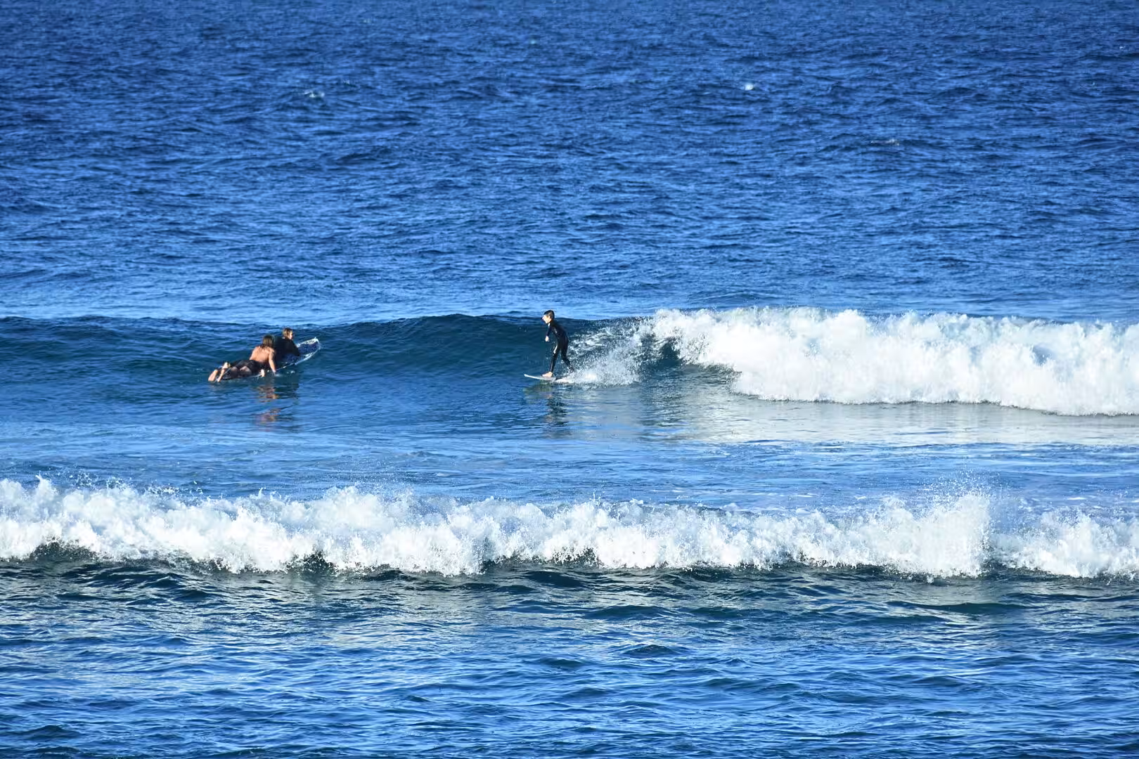 A surfer stands on a breaking wave while another waits nearby.