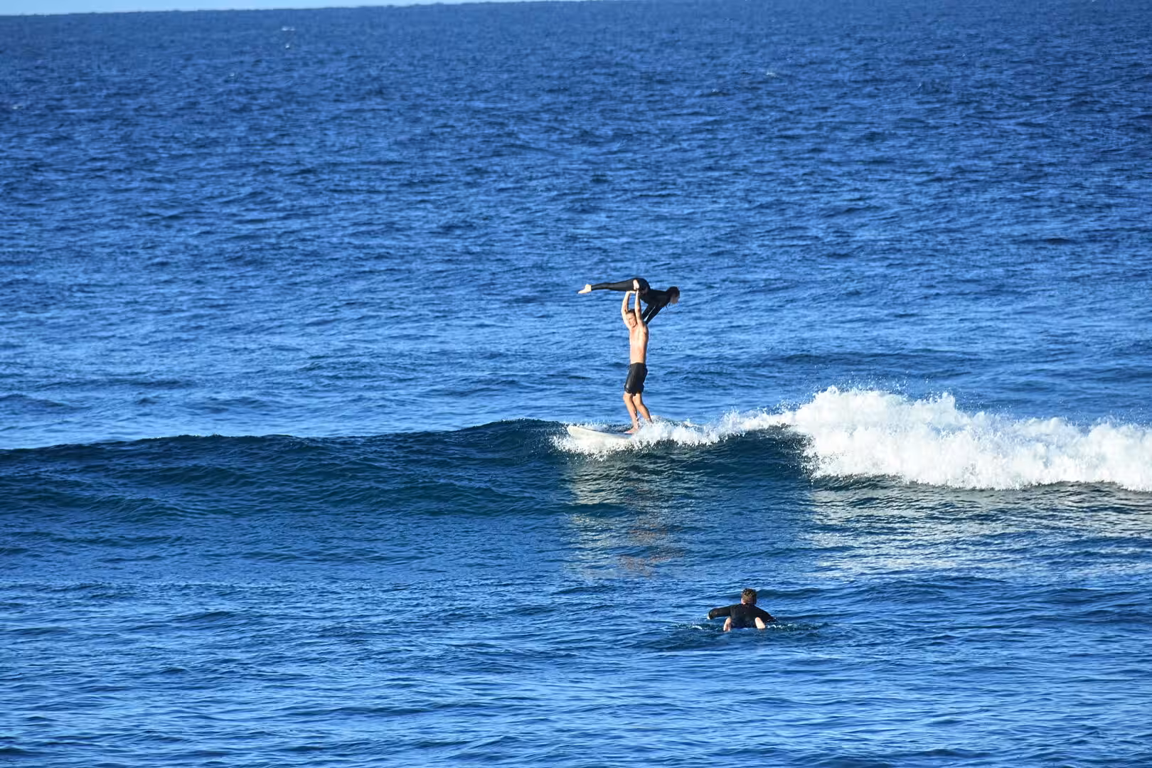 A bare-chested surfer stands with arms spread on a breaking wave.