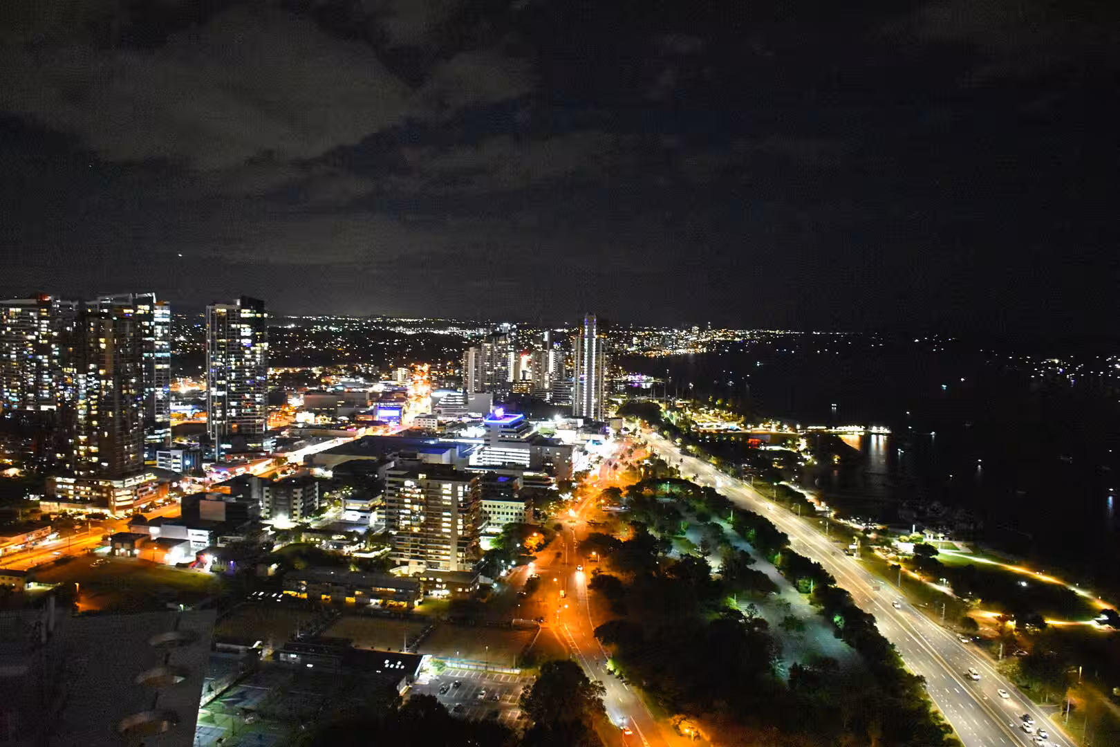 High-rise towers and a highway light up a dark waterfront at night.