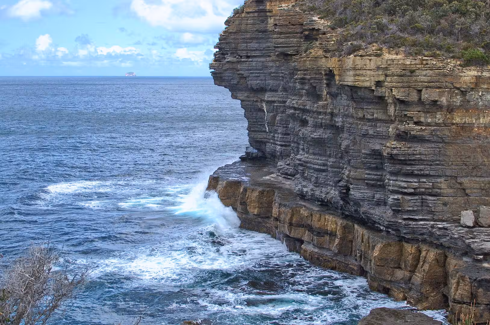 A towering sandstone cliff drops into churning blue water.