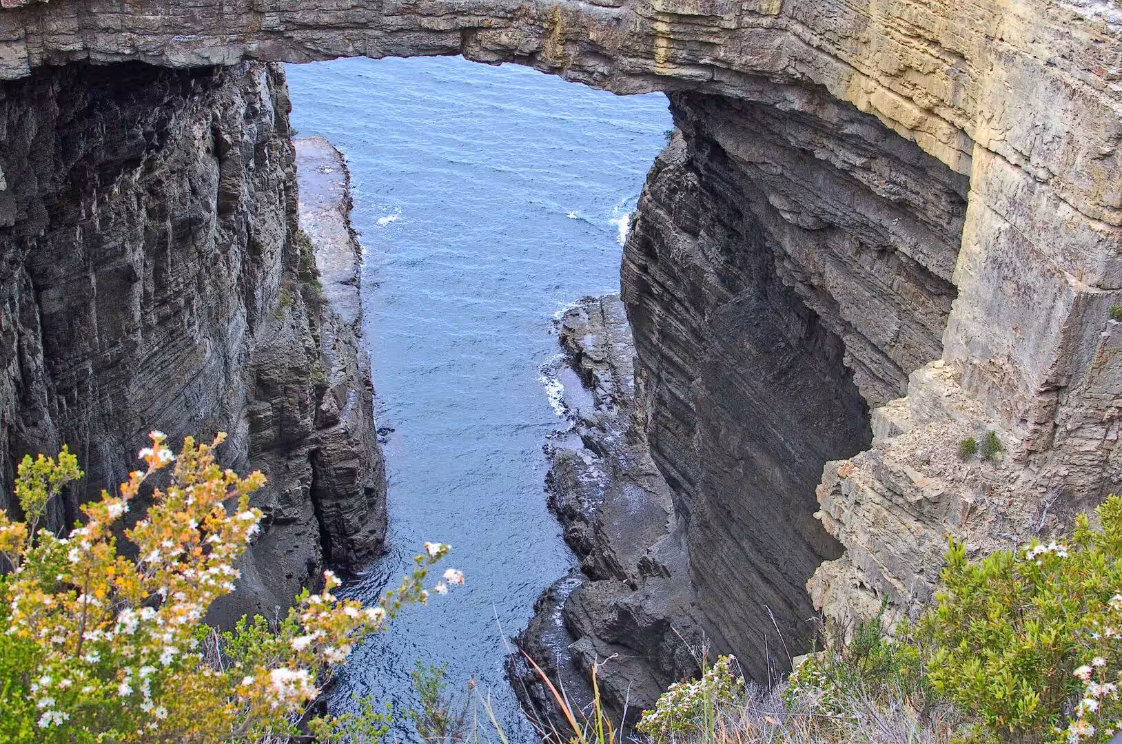 A stone arch bridges a narrow channel of seawater.