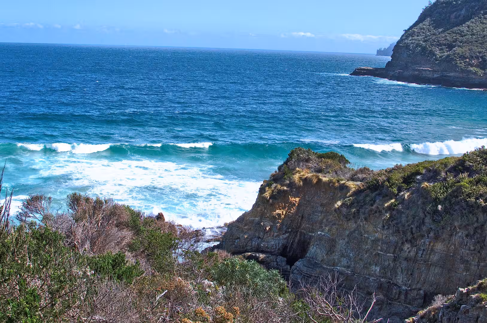 Breaking turquoise waves churn against rocky cliffs with ochre patches.