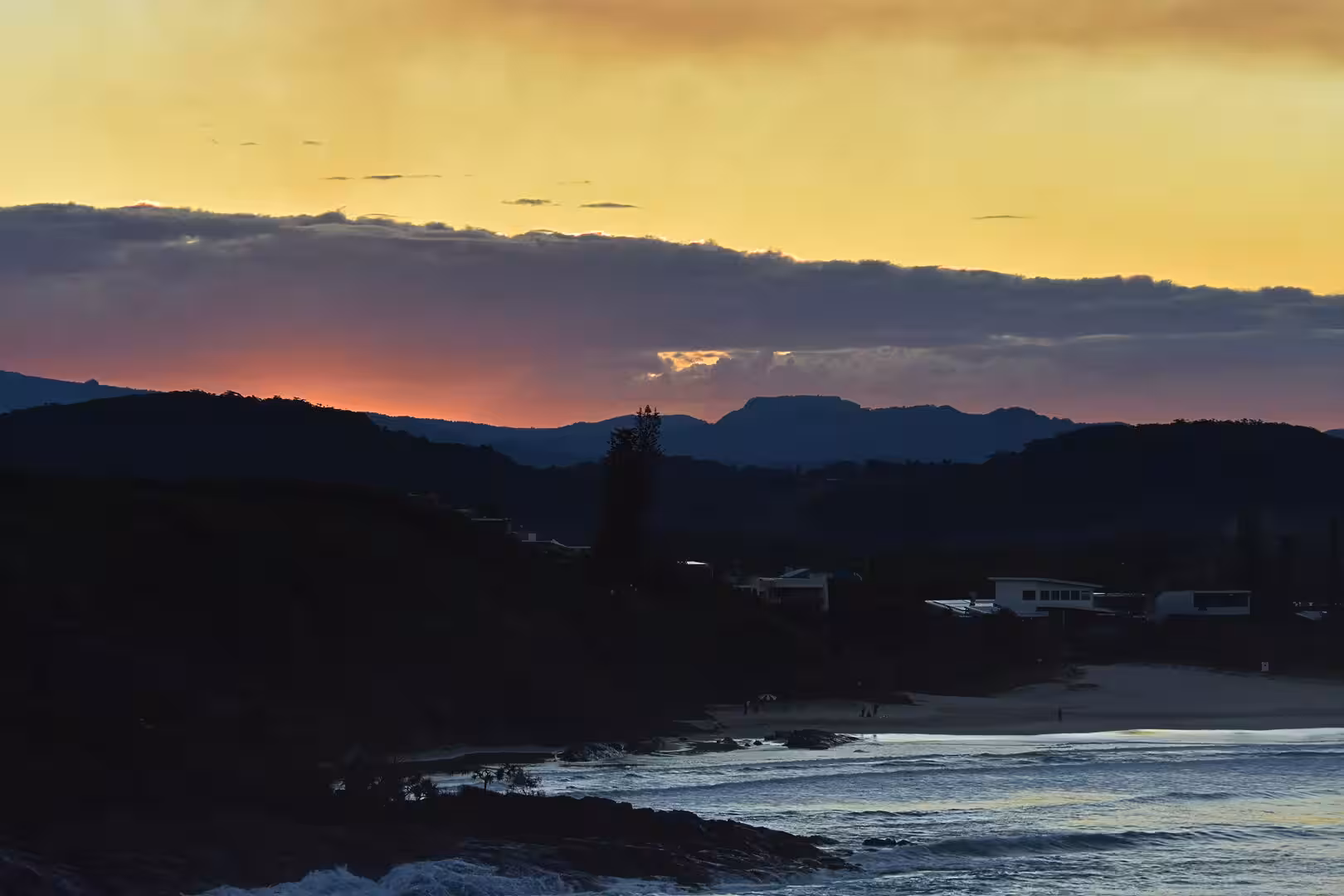 Sunset glows pink behind dark mountains and a quiet beach settlement.