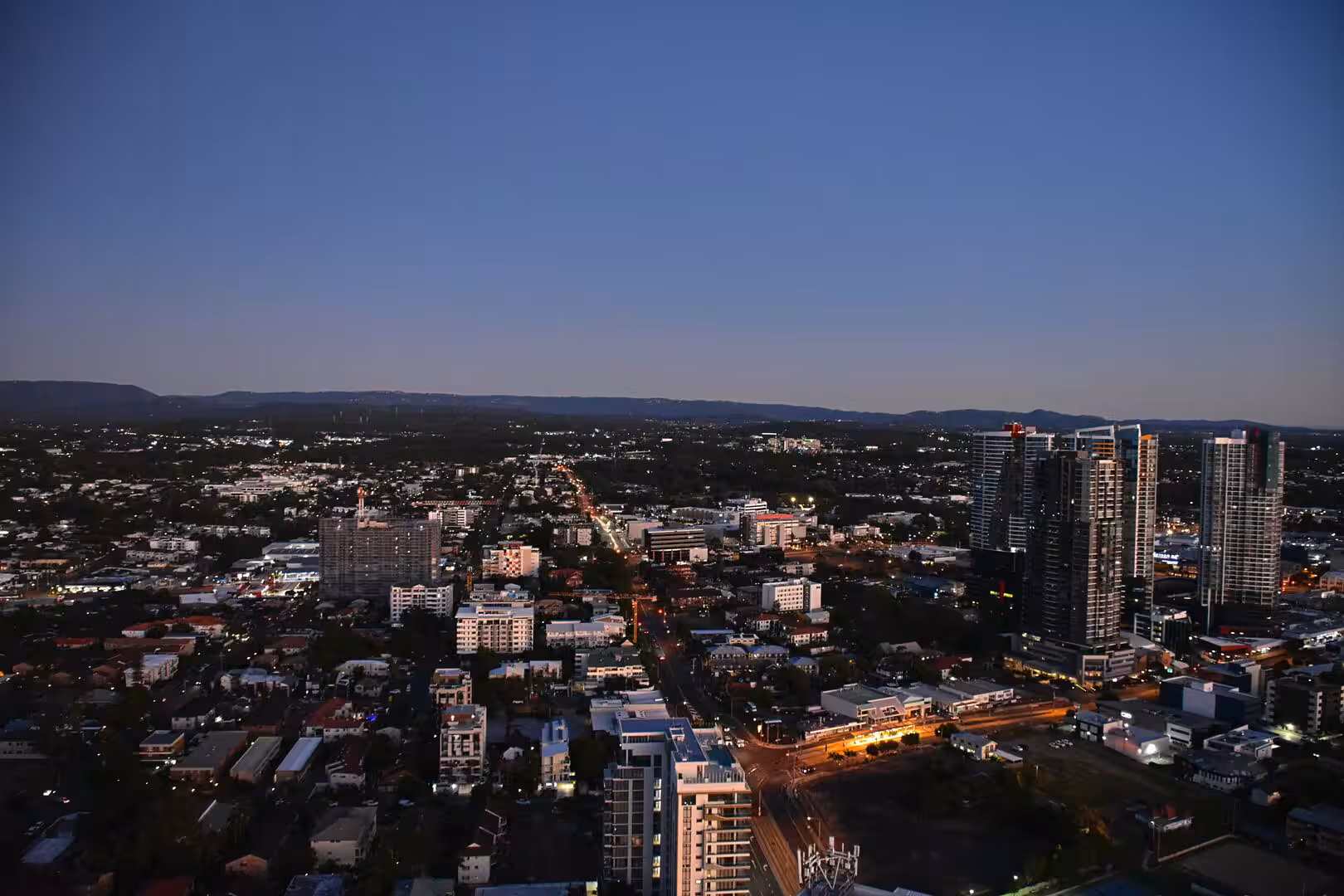 A sprawling city glows with lights beneath a deep blue twilight sky.