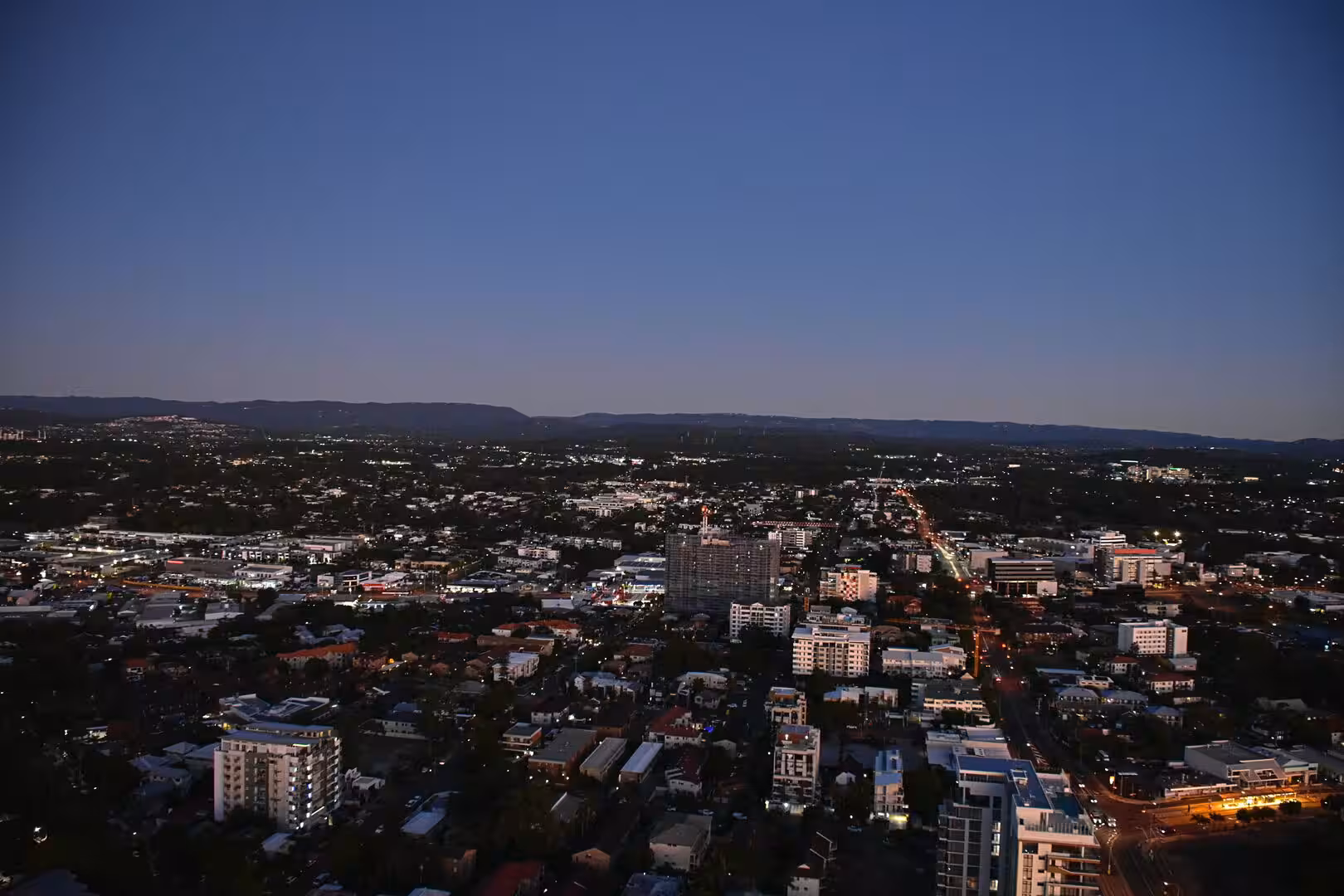 A wide view of city rooftops and apartment blocks settling into evening darkness.