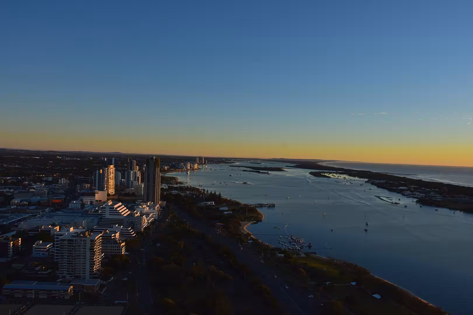 A broad estuary flows toward the sea with a high-rise skyline along its shore.