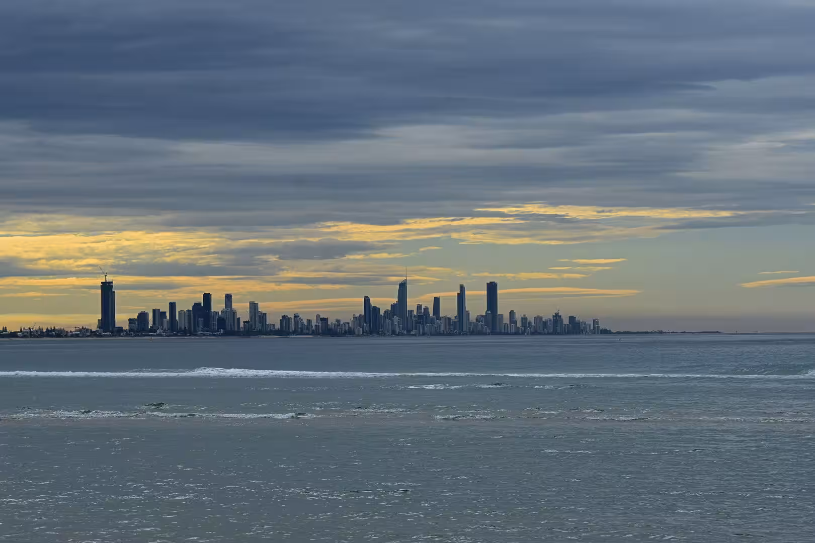 A cluster of modern high-rise towers rises across the bay under a glowing golden sky.